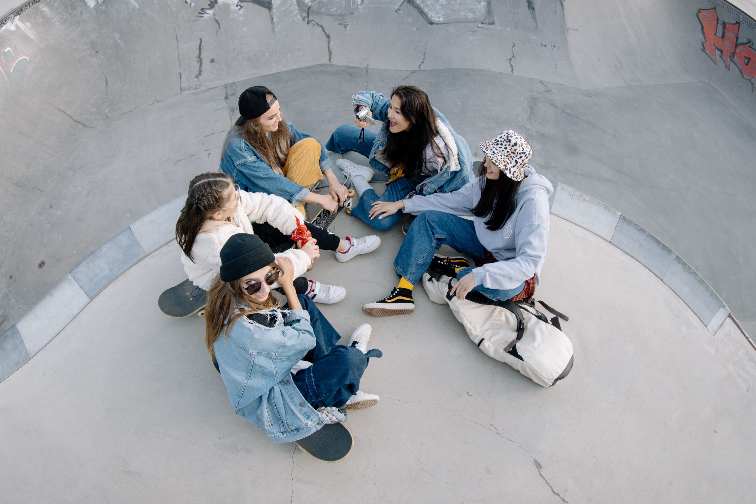 Group of young women enjoying leisure time at a skatepark, sitting with skateboards.
