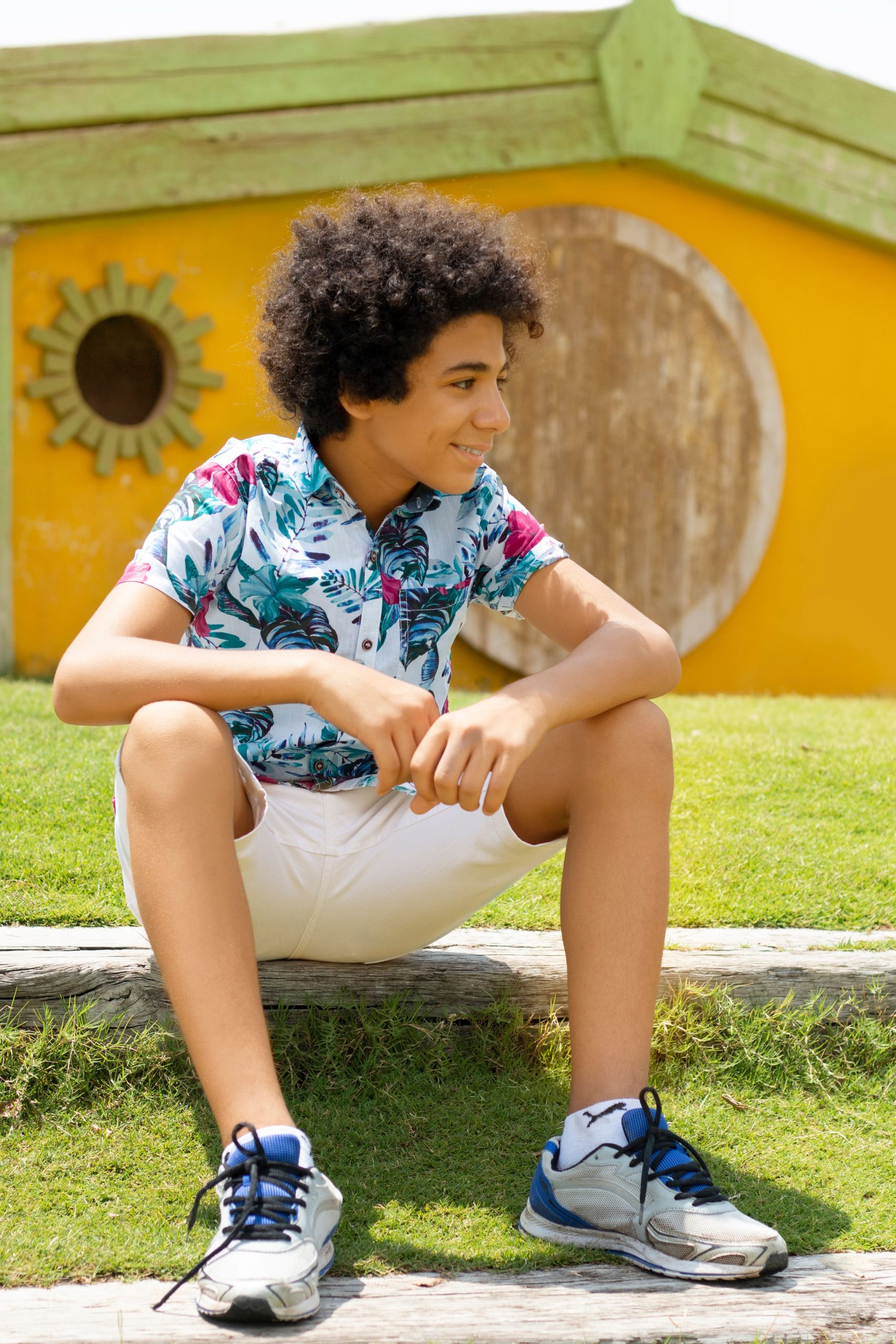 Smiling teenager sitting on a sunny day, showcasing casual fashion and joy.